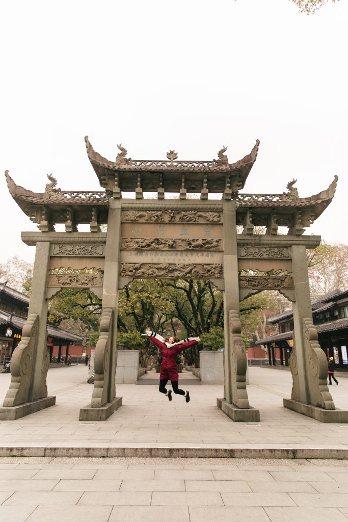 girl jumping in front of Chinese sculpture