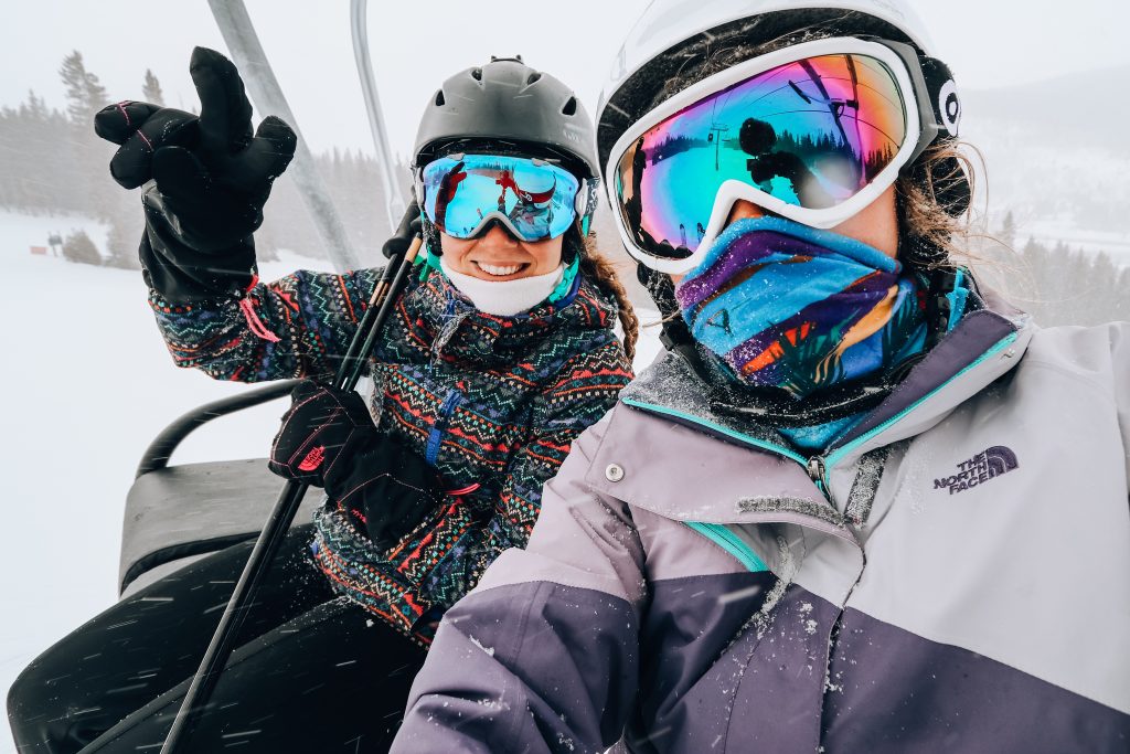 two girls riding ski lift with winter coats and goggles on